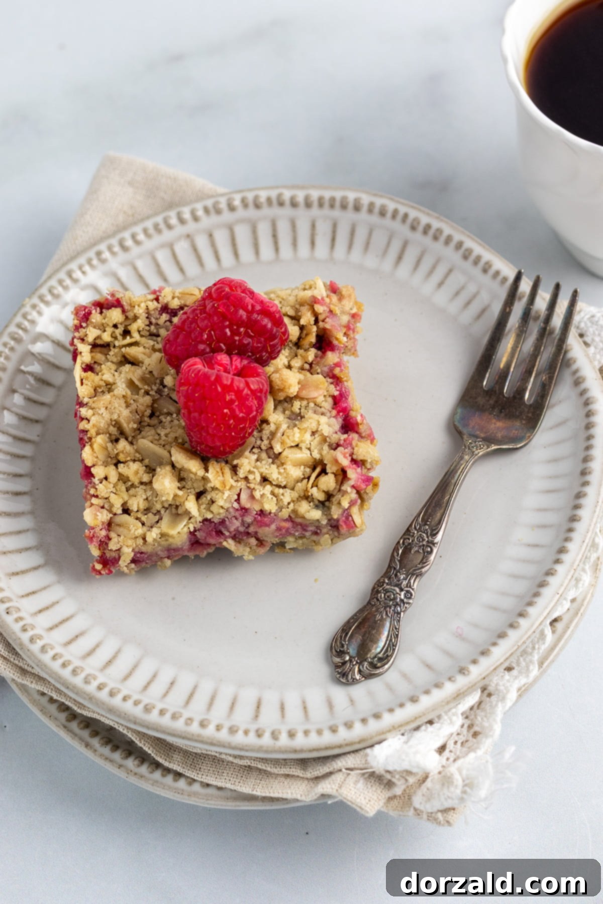 Luscious Gluten-Free Vegan Raspberry Bars 2 Gluten-free raspberry bars plated with a fork, napkin, and a cup of coffee