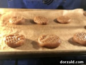Vegan Almond Butter Cookies 6 Close-up of unbaked cookie dough balls on a baking sheet, flattened and crisscrossed with a fork.