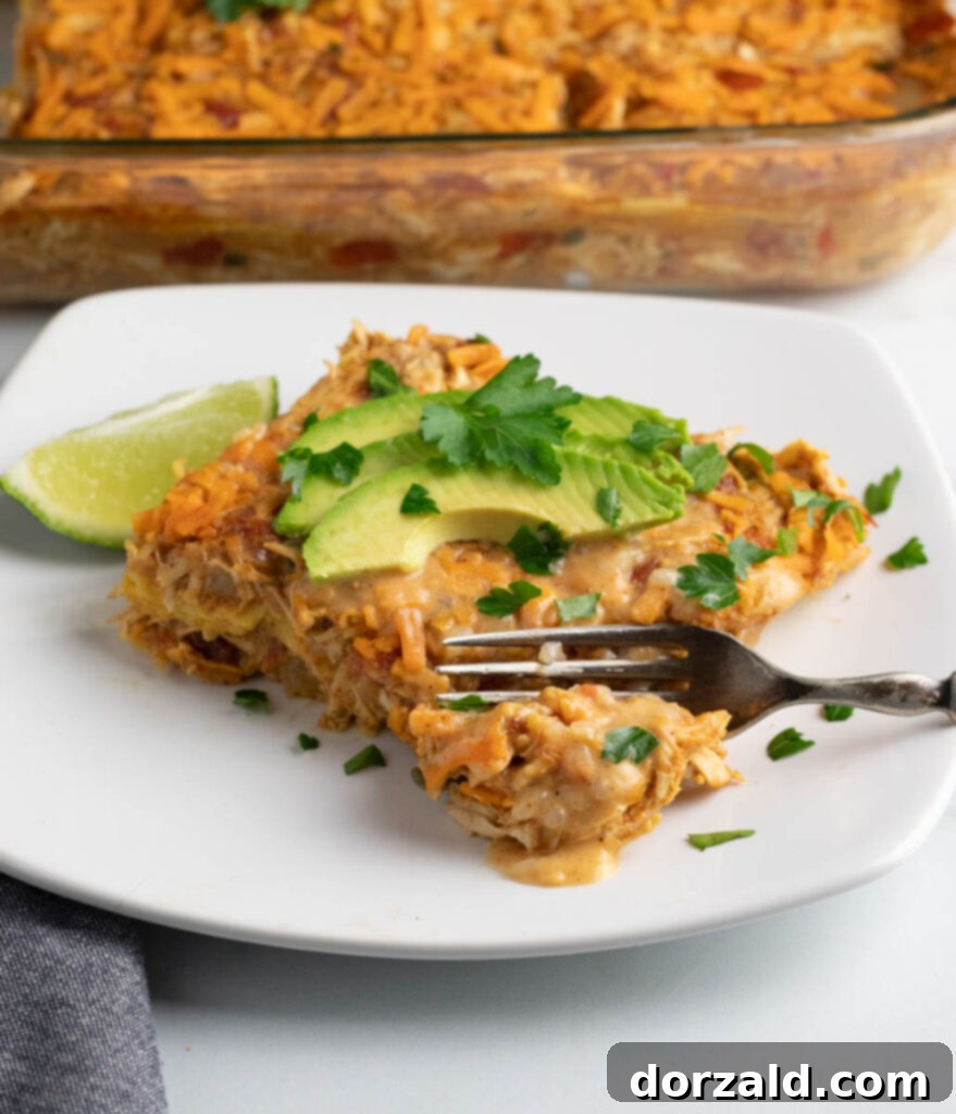 Dairy-Free King Ranch Chicken Casserole 2 A piece of dairy free chicken casserole (King Ranch style) on a white plate with a fork cutting into the first bite and the whole casserole dish behind it.