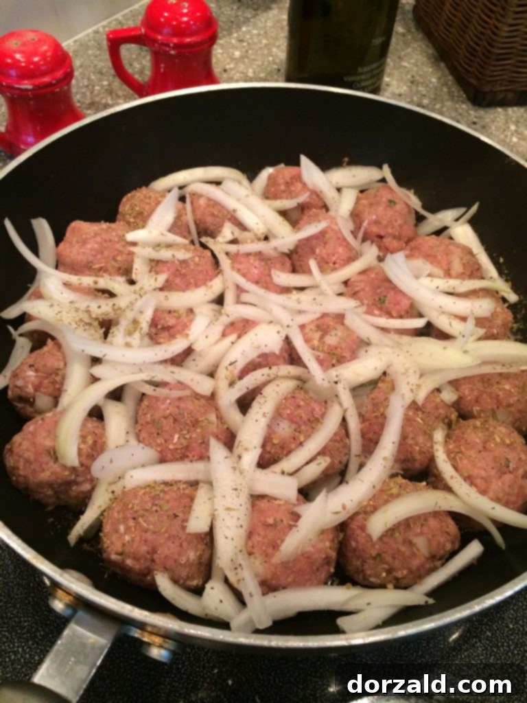 Skillet full of raw turkey meatballs topped with thinly sliced onions, prepped for cooking