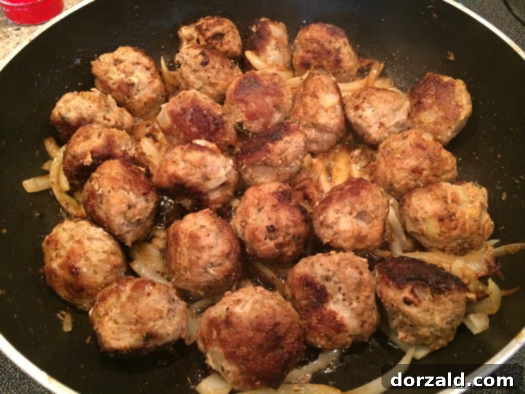 Golden-brown homemade turkey meatballs sizzling in a skillet with sautéed onions