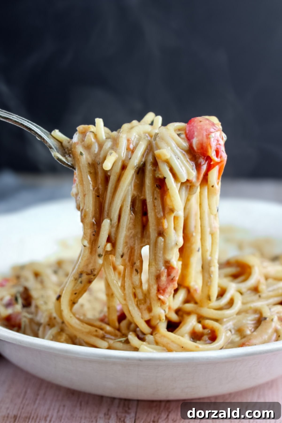 A close-up shot of vegan creamy tomato pasta with spaghetti noodles and fresh herbs.