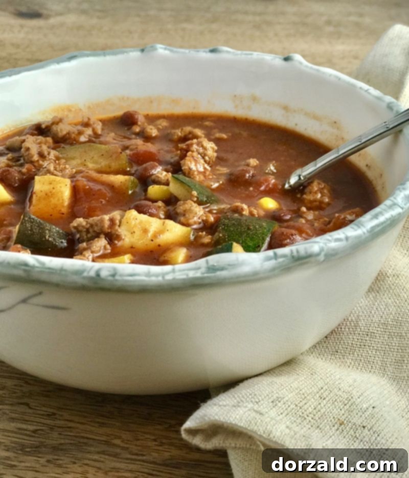 A steaming bowl of healthy Vegetable Turkey Chili garnished with fresh cilantro and cheese, ready to be enjoyed.