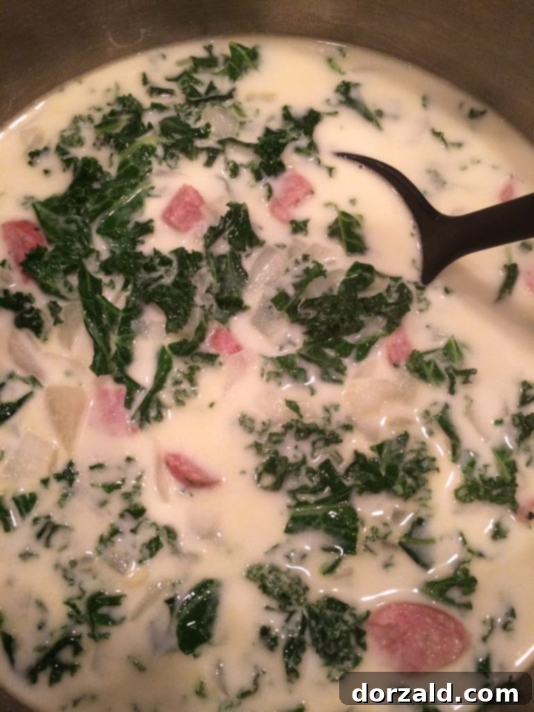 A close-up shot of a steaming bowl of Zuppa Toscana, featuring Italian sausage, tender potatoes, and vibrant kale in a creamy broth.