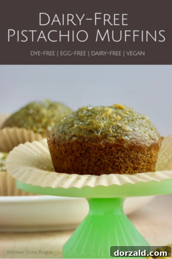 A single dairy-free pistachio muffin on a small green cupcake stand with a plate of more muffins behind it, showcasing its delicious texture and color.