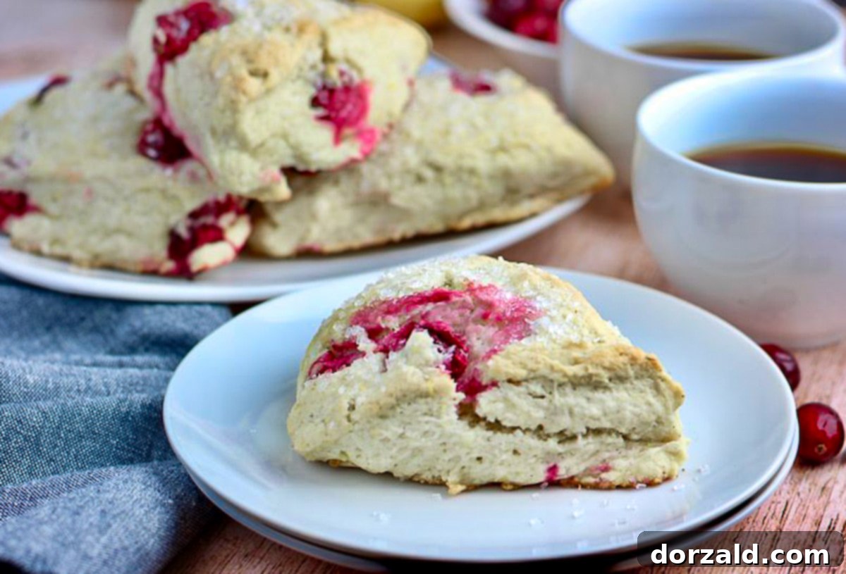 Two mugs of coffee next to a plate of freshly baked Vegan Cranberry Lemon Scones