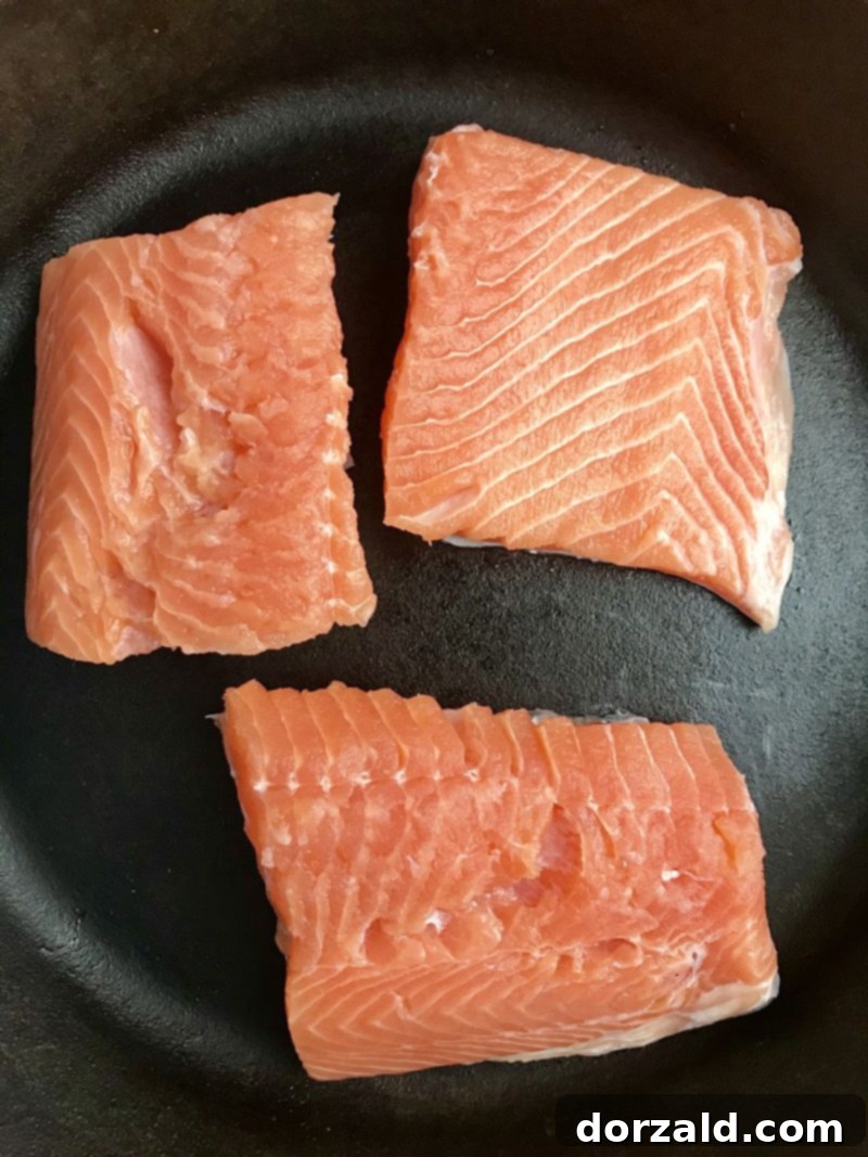 Salmon fillets placed skin-side down in a cast iron pan, ready for roasting.