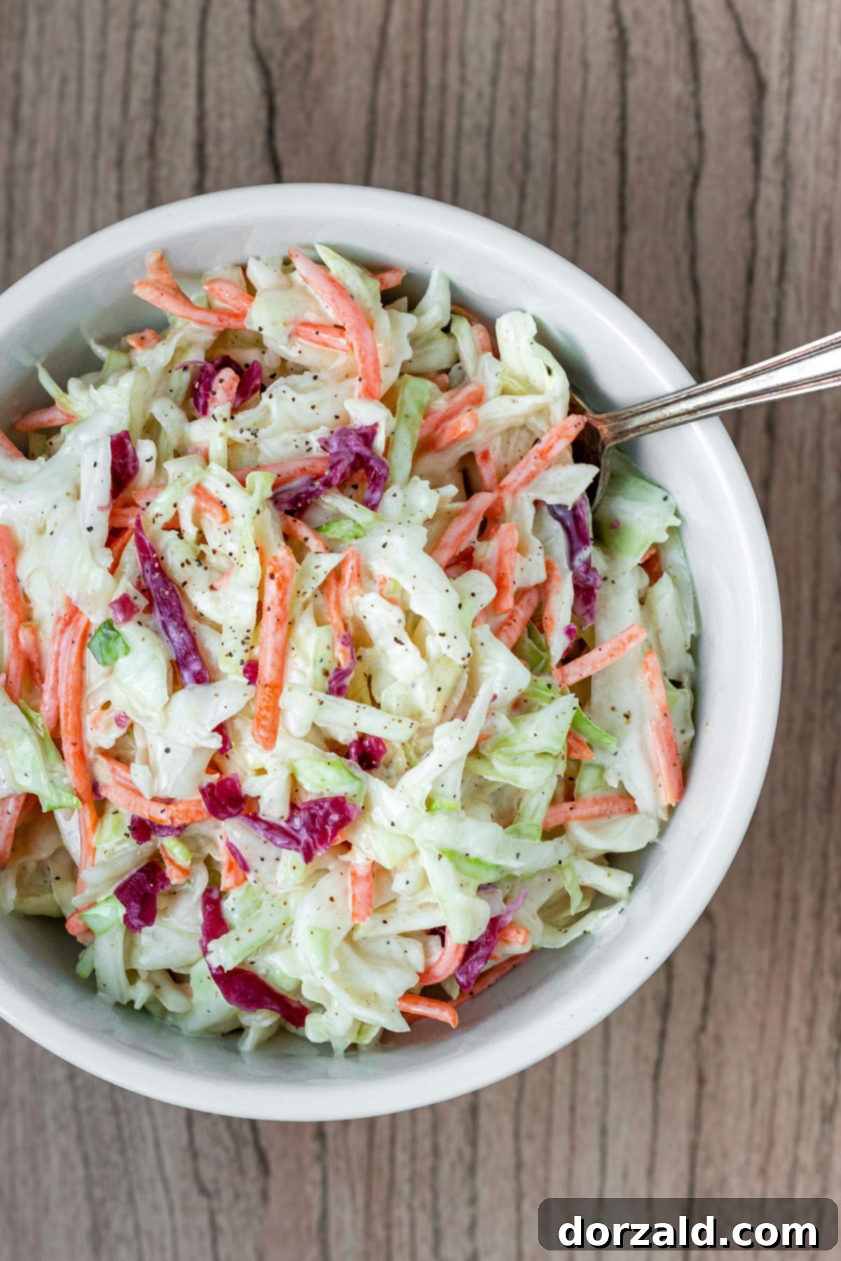 Overhead photo of a colorful easy coleslaw recipe from Kitchen Gone Rogue in a white bowl with a spoon in it, showcasing vibrant shredded cabbage and carrots.