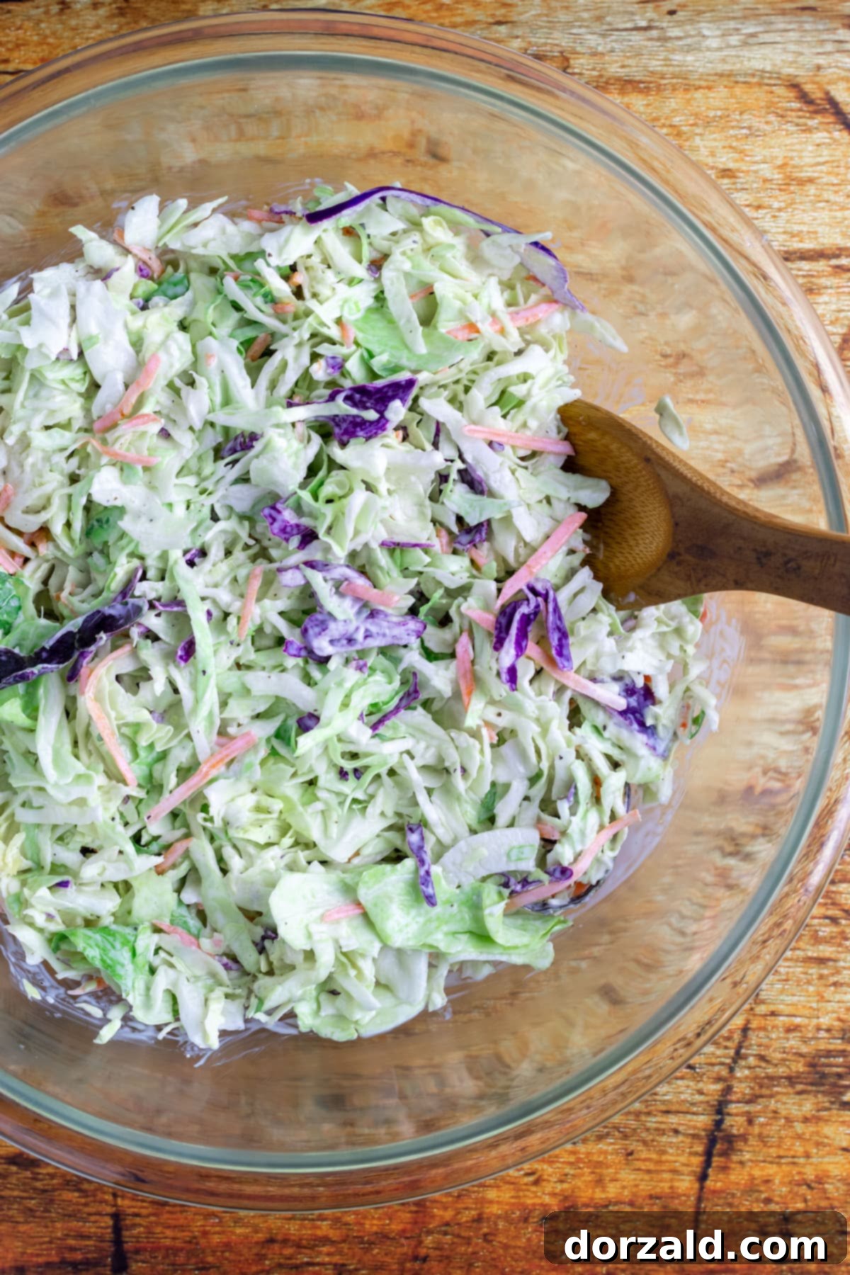 All coleslaw ingredients including dressing being mixed together in a large white bowl with a spoon, showing a well-combined and creamy texture.