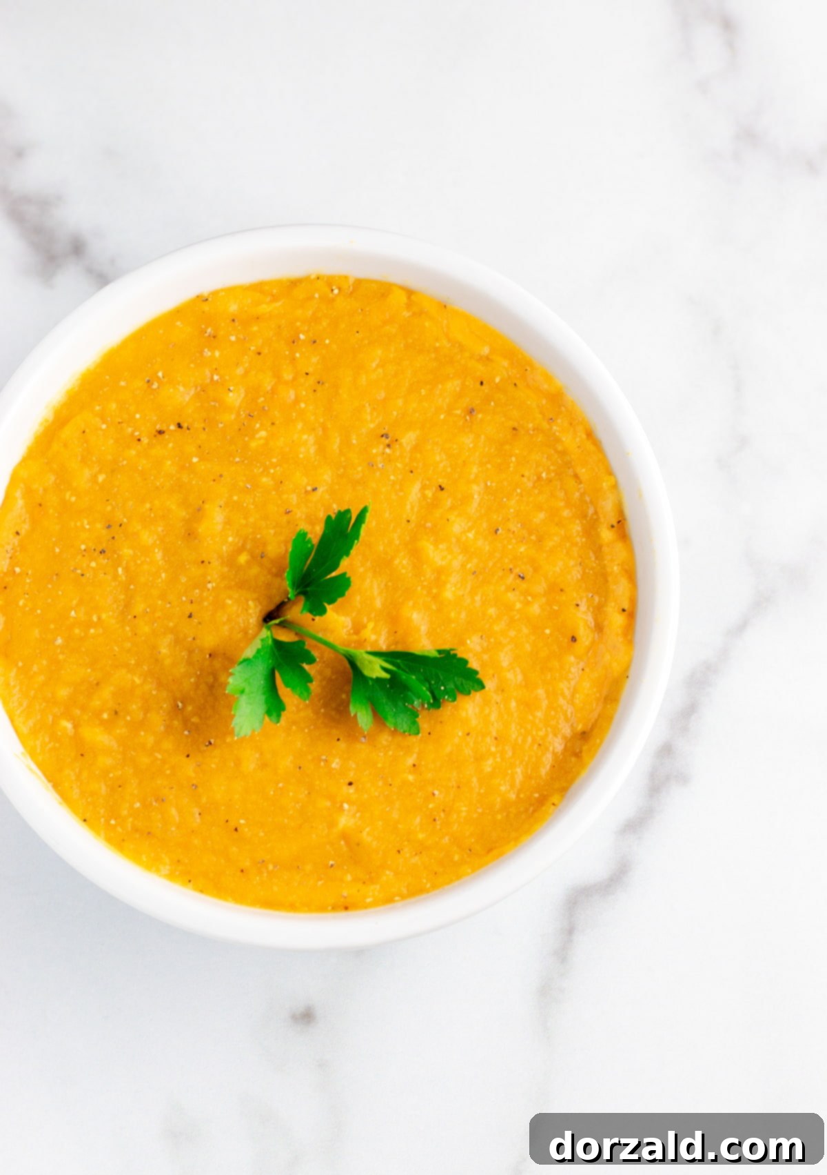 A vibrant bowl of red lentil soup with a lemon slice and fresh parsley garnish.