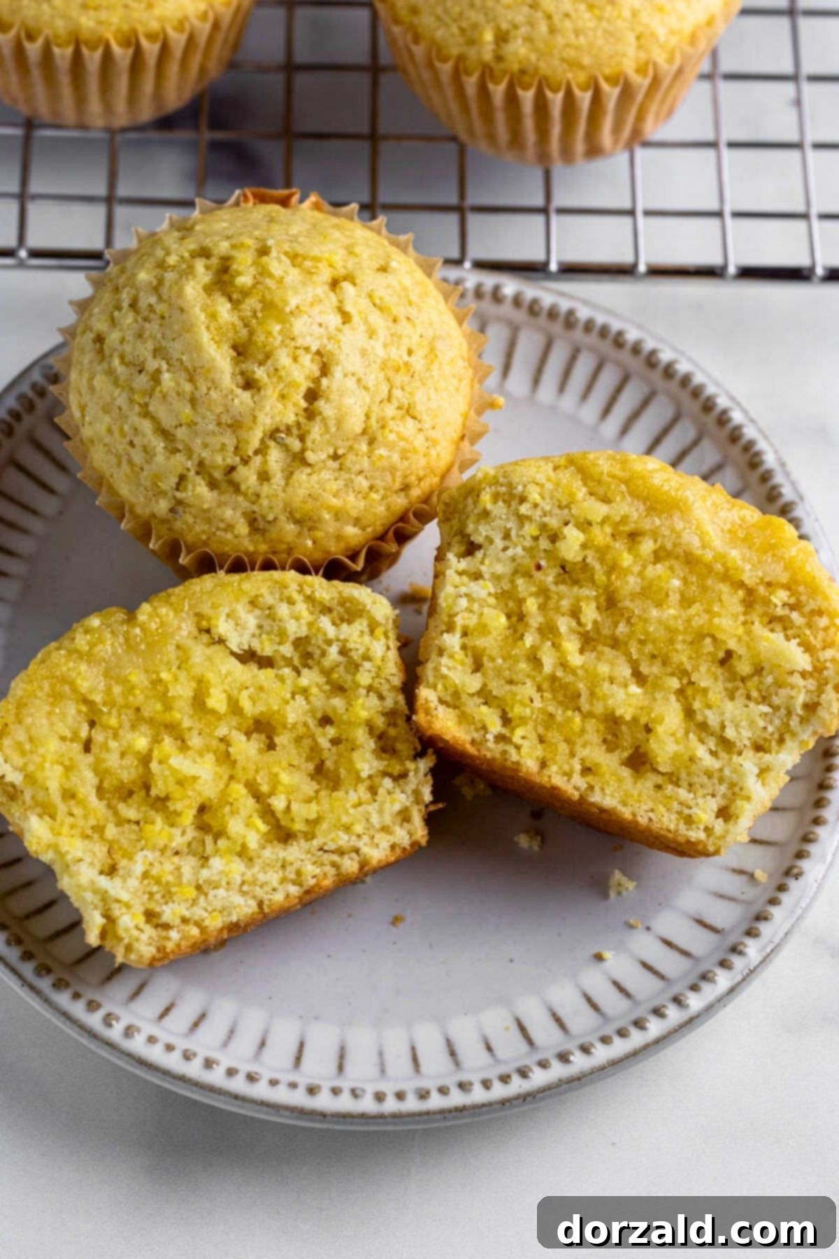 A plate of freshly baked dairy-free corn muffins, one broken open to show the fluffy interior.