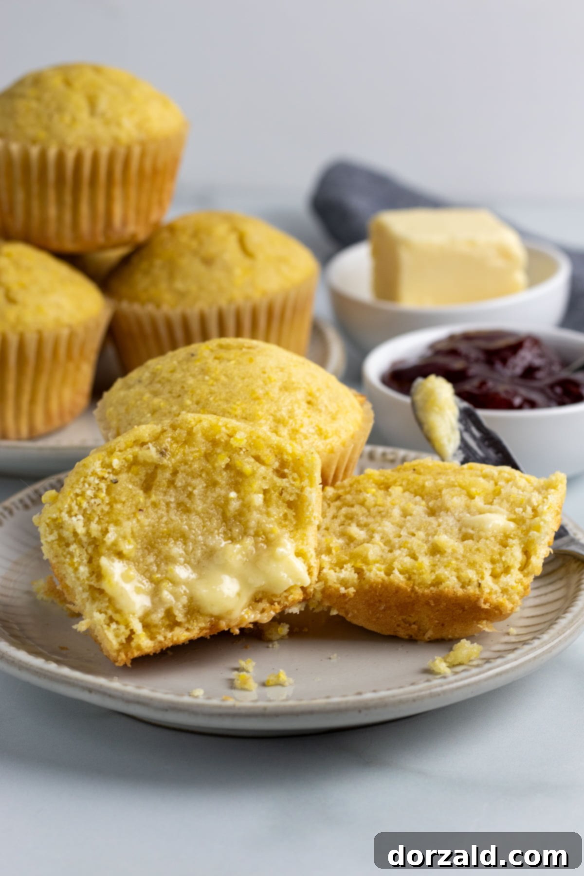 A close-up of two dairy-free corn muffins, one with a bite taken out, showing the fluffy texture.