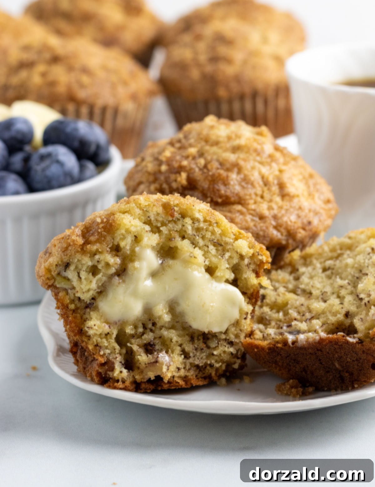 A hand reaching for a dairy-free banana muffin from a wooden board filled with freshly baked muffins.