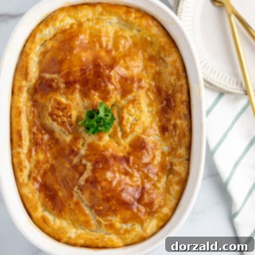 Creamy Dairy-Free Chicken Pot Pie 8 white casserole dish with dairy-free chicken pot pie in it, fresh out of the oven, sitting on white marble counterop, with a green and white striped towel and gold knife and fork beside it