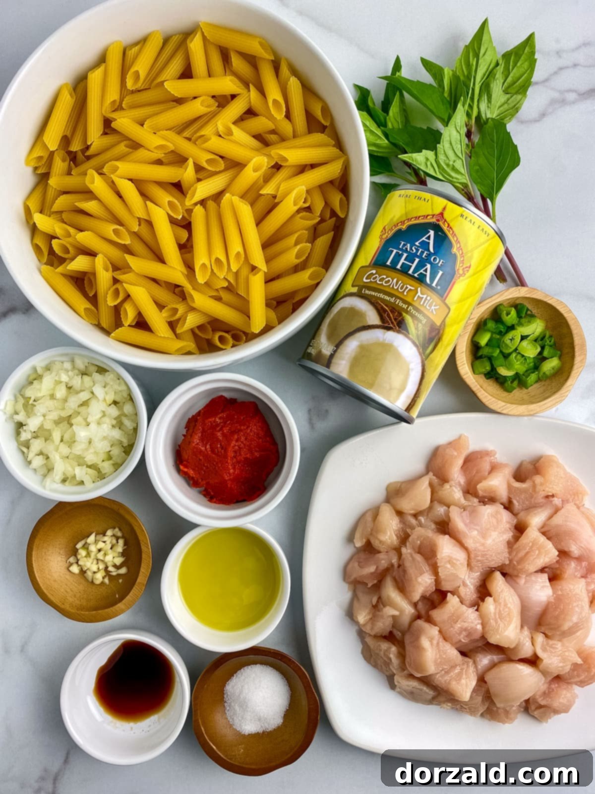 Creamy Chicken Curry Pasta 4 A selection of ingredients for the Chicken Curry Pasta recipe laid out on a wooden cutting board, including chicken, pasta, coconut milk, and curry paste.