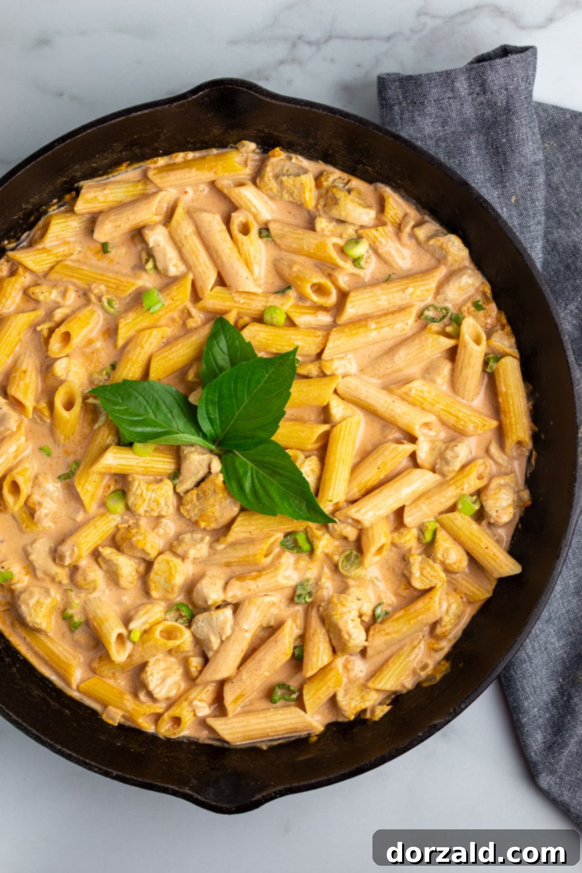 Creamy Chicken Curry Pasta 6 A serving of Chicken Curry Pasta in a rustic bowl, topped with fresh green onions and basil, ready to be eaten.