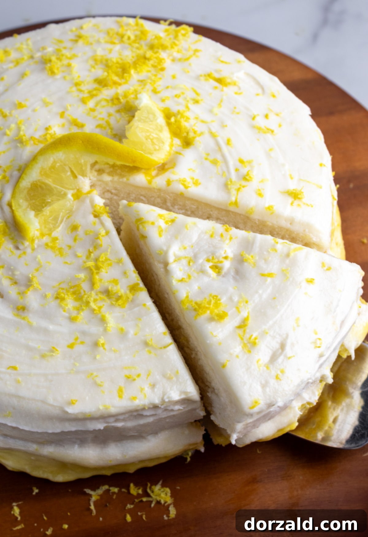 A slice of dairy-free lemon cake being served from a wooden cake stand, revealing its fluffy layers and lemon curd filling.