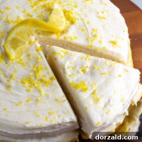 dairy-free lemon cake on wooden cake stand with on piece cut and being pulled out with a cake server utensil