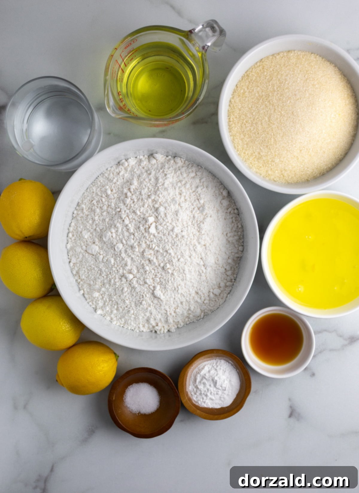 A collection of ingredients for the dairy-free lemon cake, including lemons, oil, sugar, and flour.
