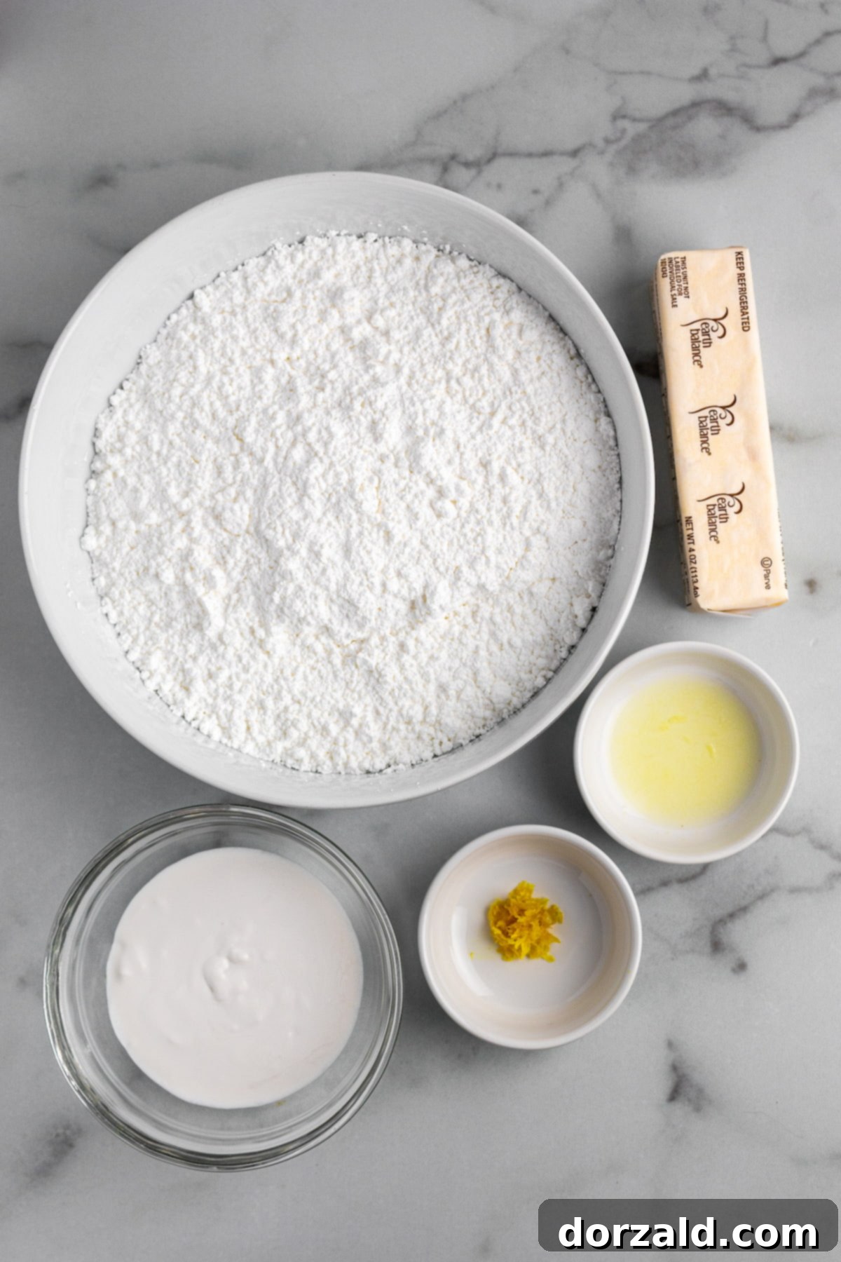 Ingredients for dairy-free lemon buttercream frosting, including lemon, vegan butter, powdered sugar, and coconut milk.