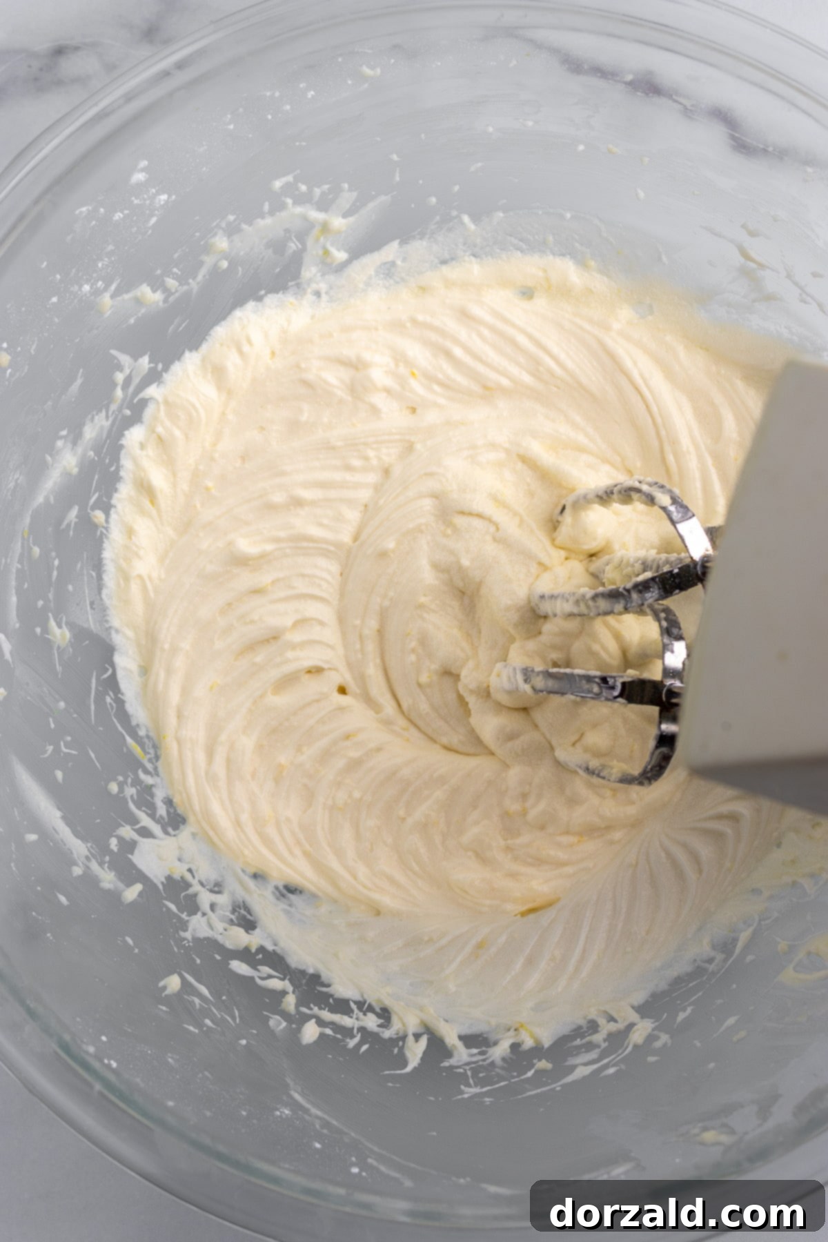 Ingredients for vegan lemon frosting being mixed in a bowl with an electric hand mixer