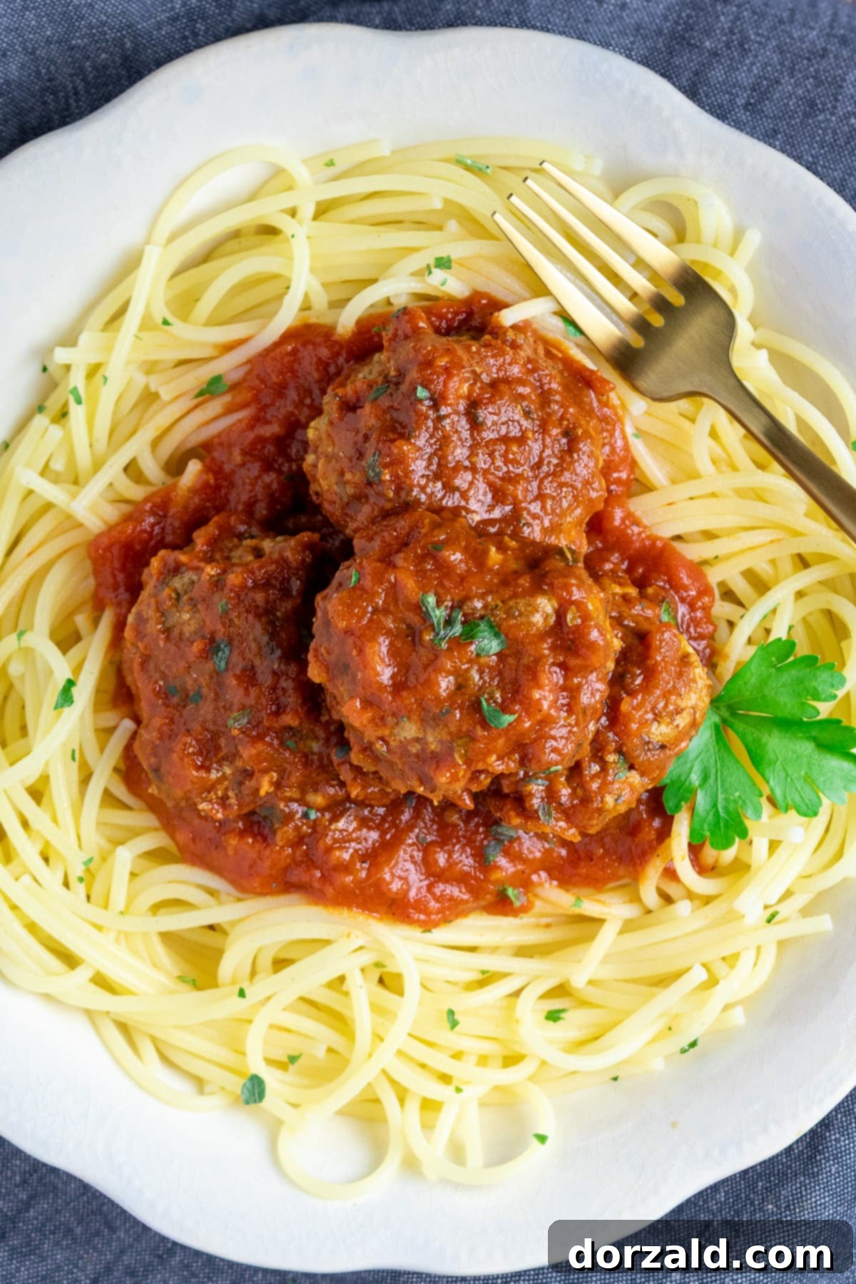 Authentic Italian Gluten-Free Dairy-Free Meatballs 2 Gluten and dairy free meatballs on top of spaghetti noodles in a white bowl with a fork, garnished with fresh parsley.