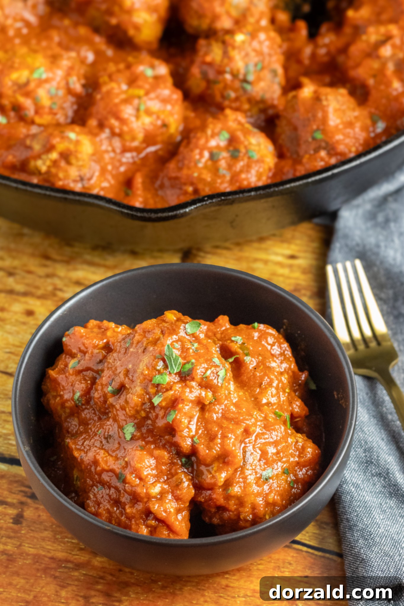 Authentic Italian Gluten-Free Dairy-Free Meatballs 6 A close-up of a single cooked gluten and dairy free meatball with marinara sauce and parsley.