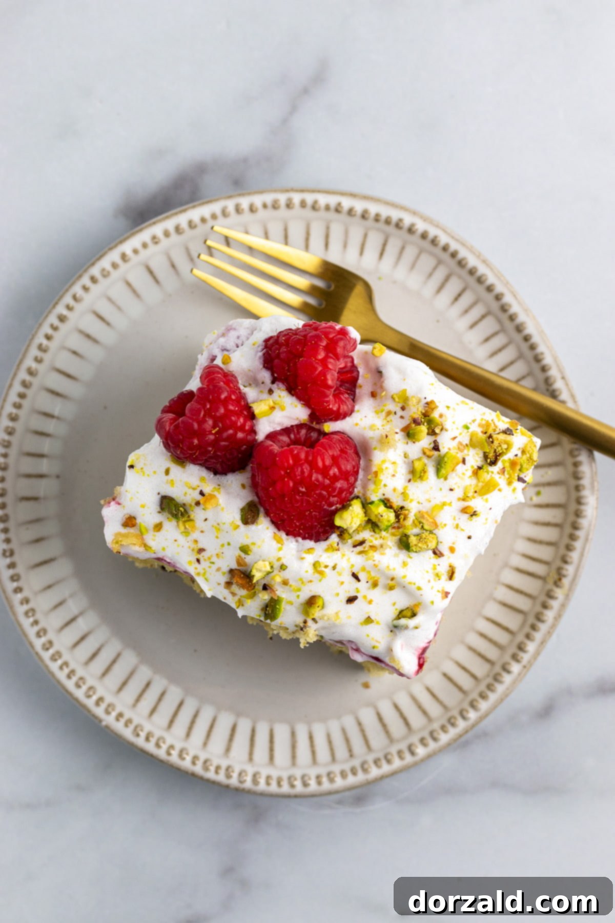Simple Pistachio Raspberry Cake 2 A slice of dairy-free pistachio raspberry cake with a vibrant raspberry layer and whipped topping.