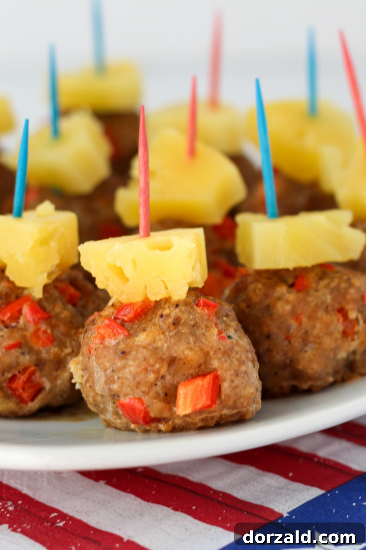 A vibrant close-up of a plate full of perfectly baked Spicy Hawaiian Turkey Meatballs, garnished with fresh pineapple chunks.